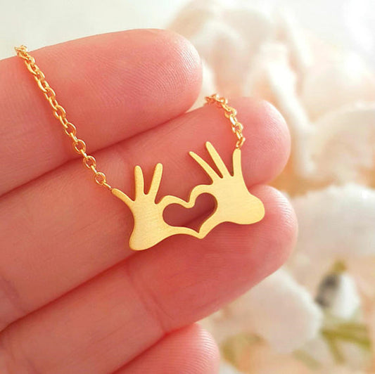 Minimalist gold and silver tone hand heart gesture pendant necklace on a sleek chain, trending K-pop aesthetic jewelry.