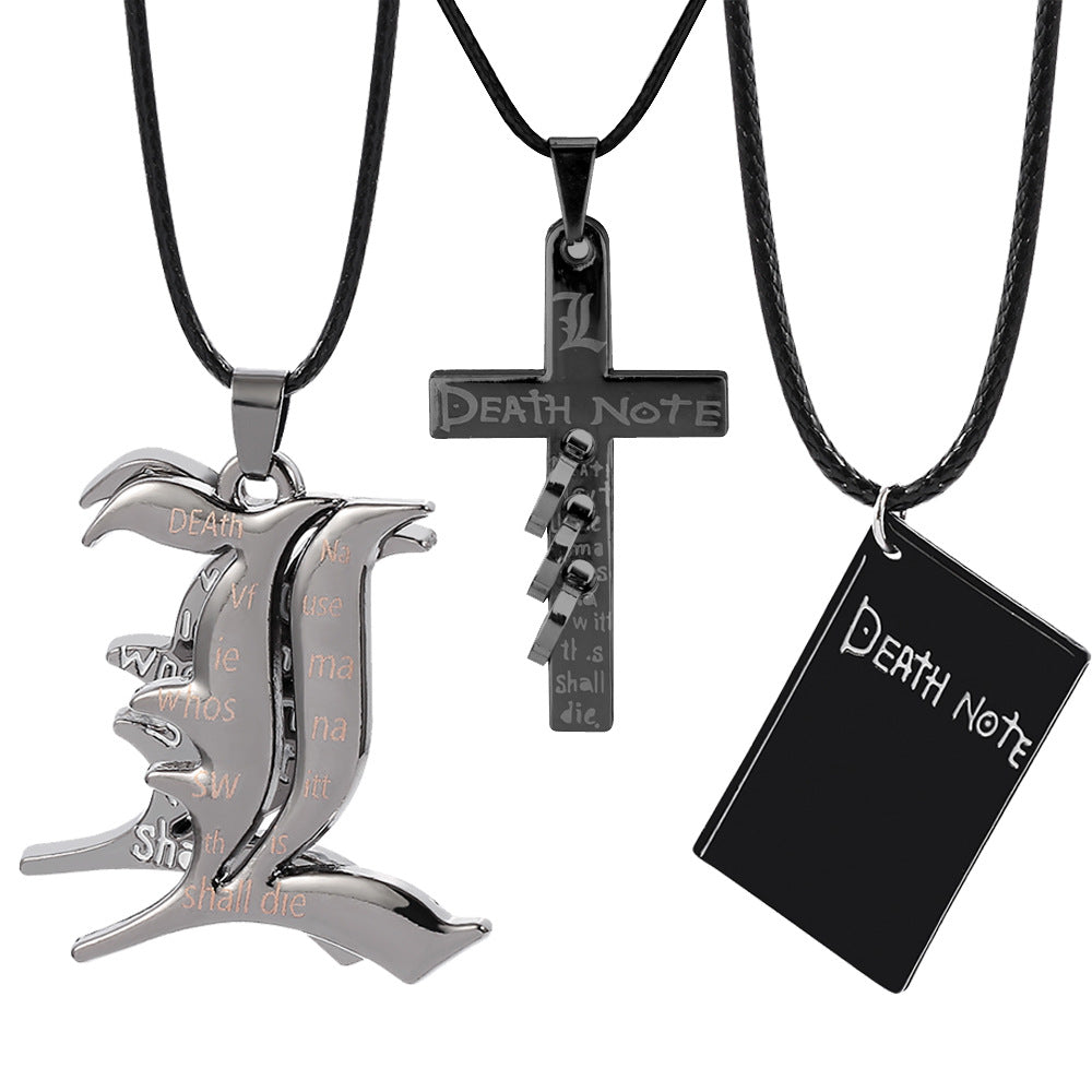 Three matte black pendants including a stylized 'L' emblem, a cross with spiral details, and a notebook charm, all suspended from minimalist black cords on a white background.