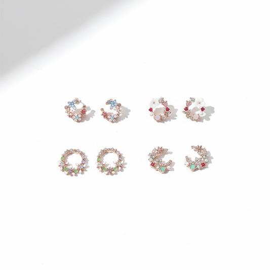 Four pairs of rose gold-tone stud earrings in delicate circular wreath and crescent shapes, featuring pastel blue, pink, and green gemstones with tiny floral accents on a bright white background.