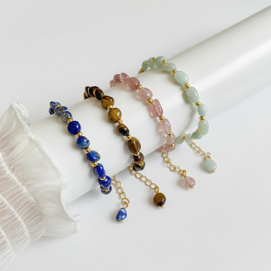 Four beaded gemstone bracelets in Lapis Lazuli, Tiger's Eye, Rose Quartz, and Amazonite with gold-tone accents and adjustable chains.