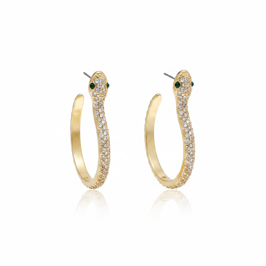 A pair of elegant 18k gold-plated snake hoop earrings featuring shimmering white crystal pavé and striking green emerald-style eyes on a white reflective background.