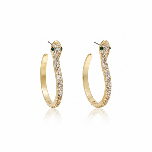 A pair of elegant 18k gold-plated snake hoop earrings featuring shimmering white crystal pavé and striking green emerald-style eyes on a white reflective background.