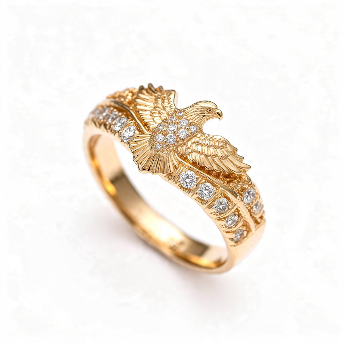 A polished gold ring with a detailed eagle in flight and pavé crystal accents along the band, centered on a pure white background.