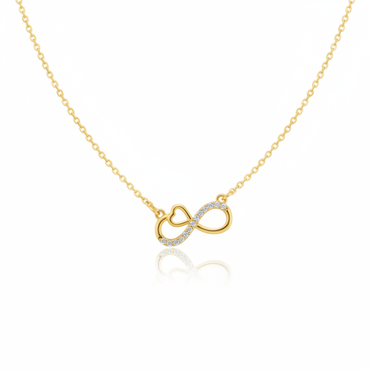 A gold-toned necklace featuring an infinity symbol pendant with an integrated heart detail. One side of the infinity loop is pavé-set with shimmering clear crystals. The pendant is attached to a fine gold cable chain and shown against a white background with a subtle reflection.