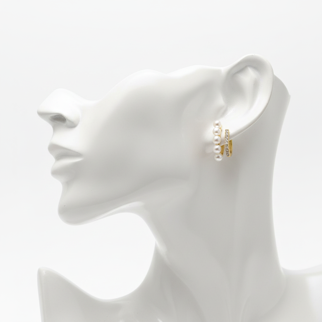 A high-resolution product shot of gold-toned hoop earrings featuring a unique double-band design; one band is lined with small white pearls and the other is pavé-set with sparkling crystals, displayed on a white mannequin bust.