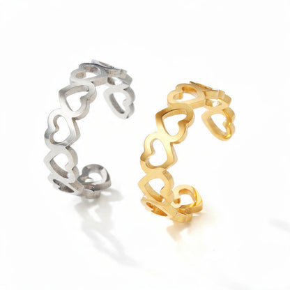 Two adjustable open rings with heart-shaped cutouts, one in polished silver and one in polished gold, displayed side by side on a pure white background.