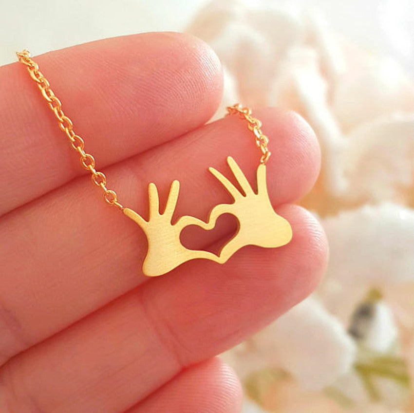 Minimalist gold and silver tone hand heart gesture pendant necklace on a sleek chain, trending K-pop aesthetic jewelry.