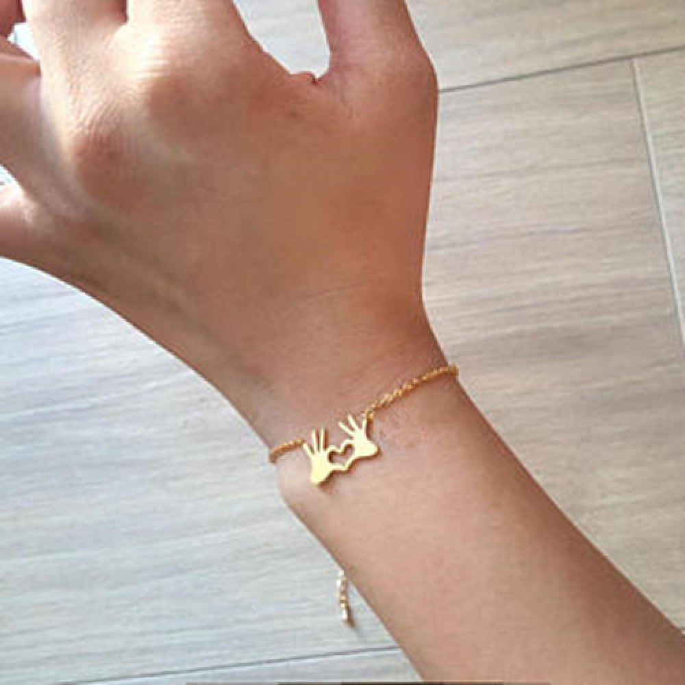 Minimalist gold bracelet featuring a hand heart gesture pendant on a dainty copper chain.