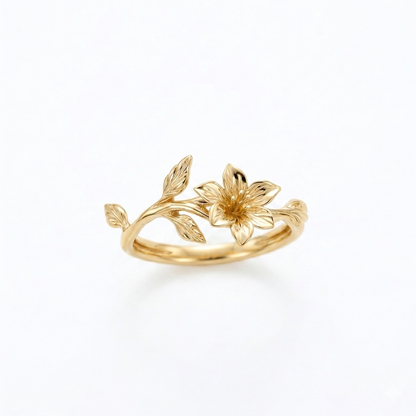 A delicate yellow gold ring with a single sculpted lily flower and an organic vine of leaves, set against a seamless white background.