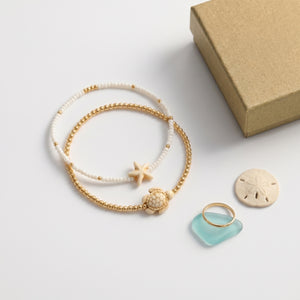 MR BATZ luxury beaded bracelet set featuring a neutral dopamine stone turtle and starfish charm, paired with a gold ring and sea glass in a warm, art gallery aesthetic.
