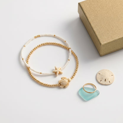 MR BATZ luxury beaded bracelet set featuring a neutral dopamine stone turtle and starfish charm, paired with a gold ring and sea glass in a warm, art gallery aesthetic.