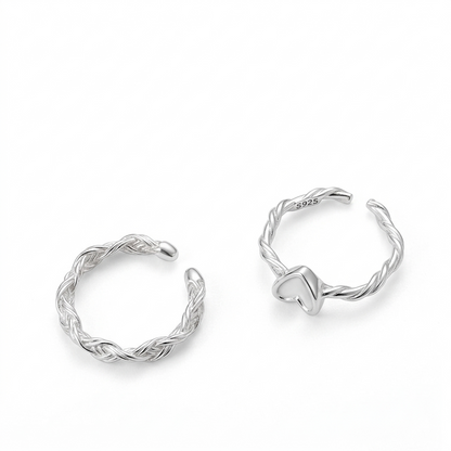 Two sterling silver adjustable rings, one braided-style band and one heart-motif twisted-band, on a pure white background.