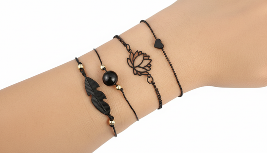 Stacked set of 4 matte black bracelets featuring a lotus flower, feather charm, and heart detail on a wrist
