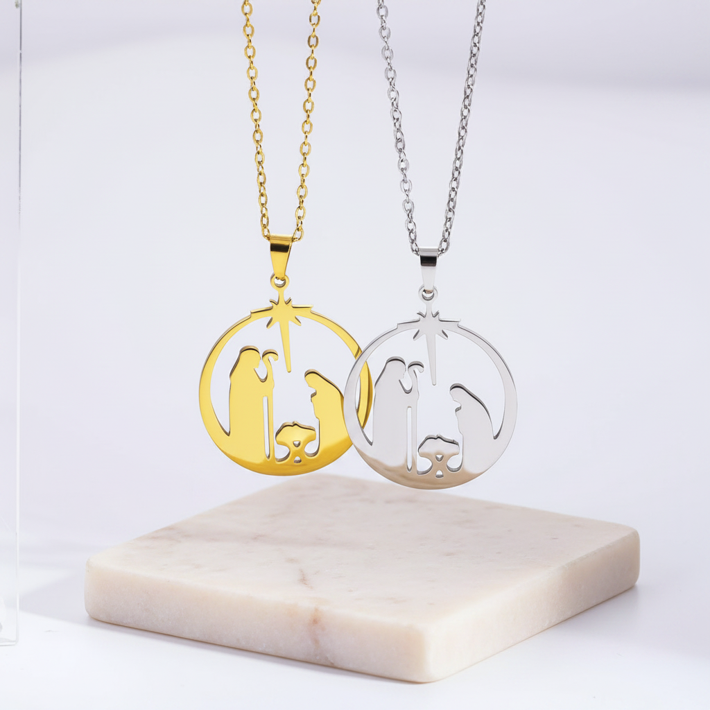 Two circular pendant necklaces featuring a laser-cut minimalist nativity scene under the Star of Bethlehem. One pendant is finished in polished gold and the other in silver. Both are suspended from matching cable chains and displayed above a natural textured stone base on a white background.
