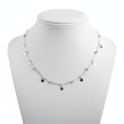 A high-resolution, close-up shot of a delicate sterling silver choker necklace featuring a thin link chain adorned with small polished silver beads and hanging circular disc charms, displayed on a clean white jewelry mannequin against a pure white background.