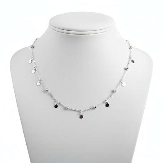 A high-resolution, close-up shot of a delicate sterling silver choker necklace featuring a thin link chain adorned with small polished silver beads and hanging circular disc charms, displayed on a clean white jewelry mannequin against a pure white background.