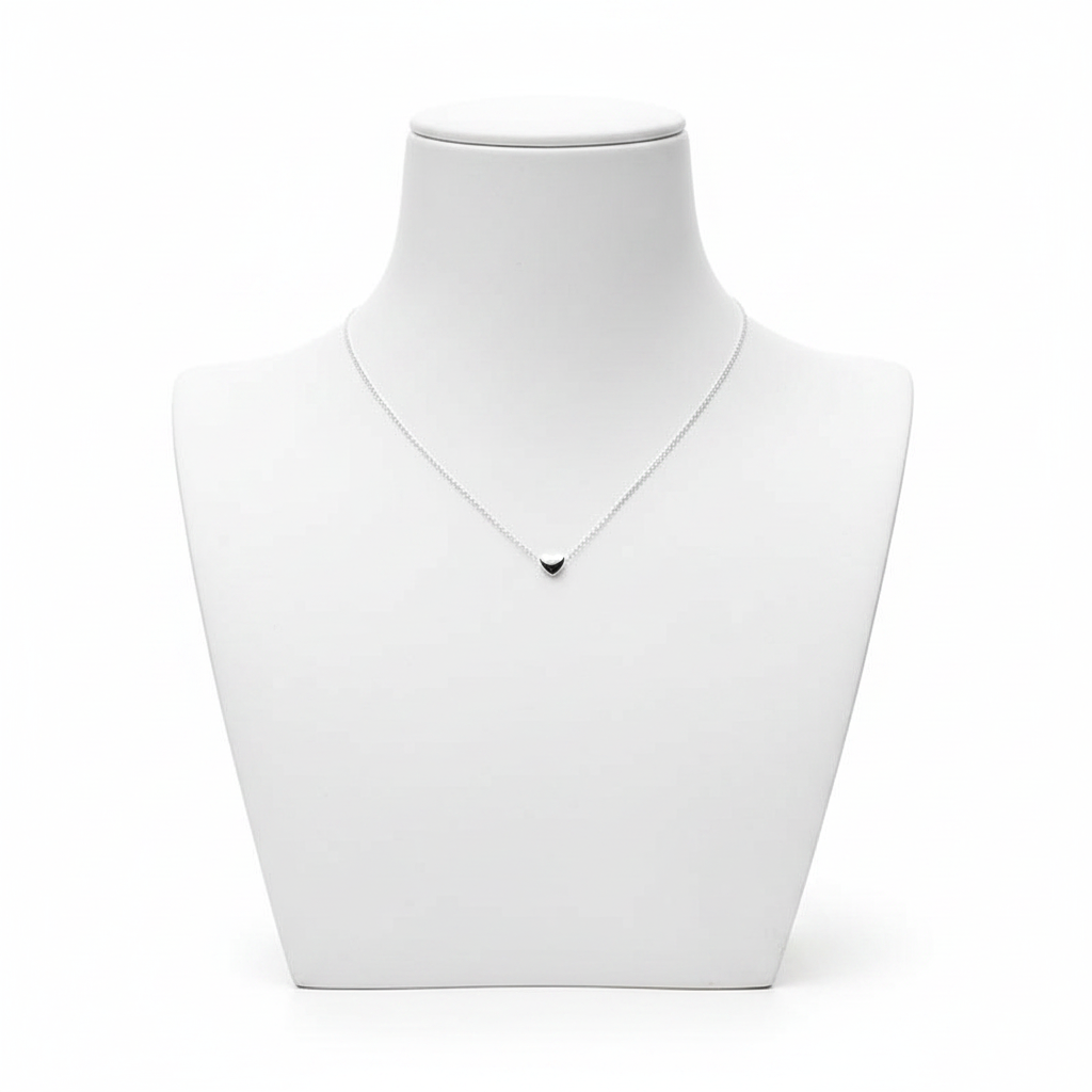 A high-resolution product shot of a minimalist silver necklace with a tiny, solid heart-shaped pendant on a fine link chain, displayed on a clean white jewelry bust against a pure white background.
