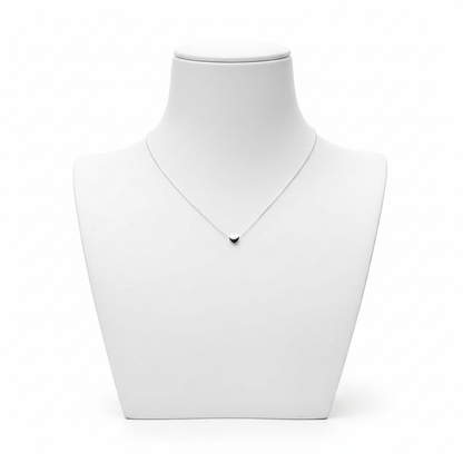 A high-resolution product shot of a minimalist silver necklace with a tiny, solid heart-shaped pendant on a fine link chain, displayed on a clean white jewelry bust against a pure white background.