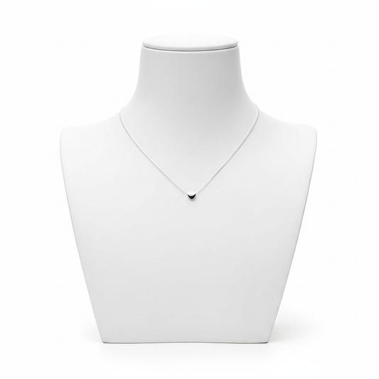 A high-resolution product shot of a minimalist silver necklace with a tiny, solid heart-shaped pendant on a fine link chain, displayed on a clean white jewelry bust against a pure white background.