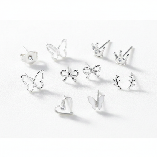 A high-resolution product shot of a collection of dainty sterling silver stud earrings in various shapes, including butterflies, crowns with small crystals, bows, antlers, and a heart, all displayed on a clean white surface.