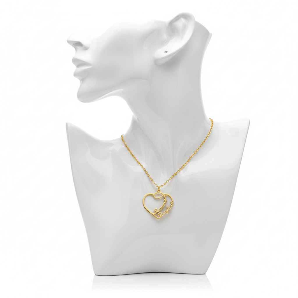 A high-resolution product shot of a personalized gold-plated necklace featuring a large open-heart pendant with two script names entwined within the design, displayed on a sleek white bust mannequin against a pure white background.
