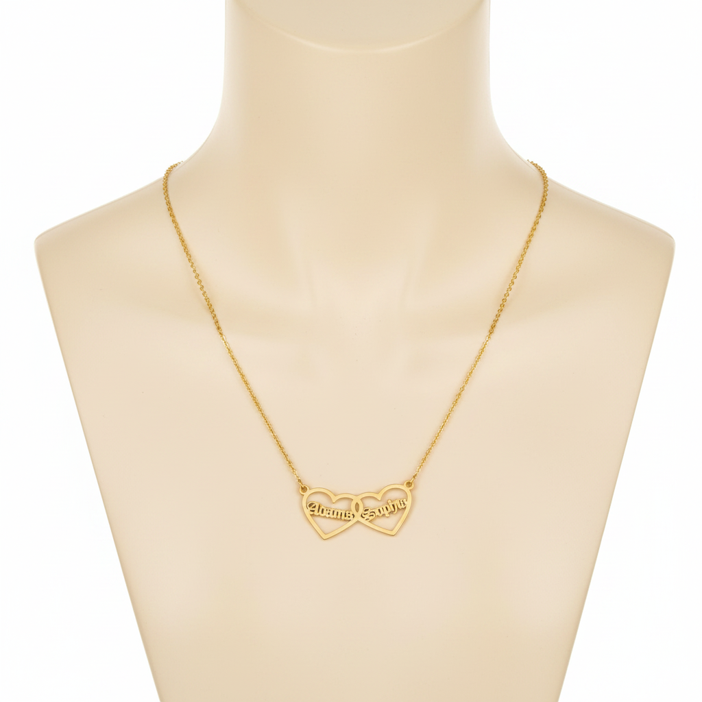 A gold-toned necklace featuring two interlocking open-heart pendants, displayed on a beige mannequin bust. Each heart is personalized with a name in a Gothic-style font: "Alonma" on the left and "Sophia" on the right. The pendant is attached to a fine gold cable chain.
