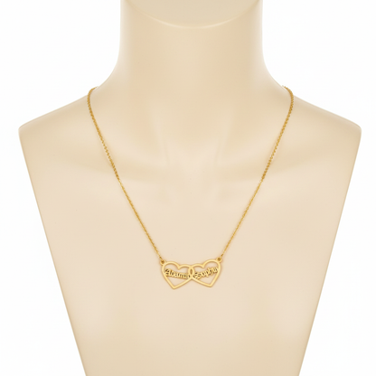 A gold-toned necklace featuring two interlocking open-heart pendants, displayed on a beige mannequin bust. Each heart is personalized with a name in a Gothic-style font: "Alonma" on the left and "Sophia" on the right. The pendant is attached to a fine gold cable chain.