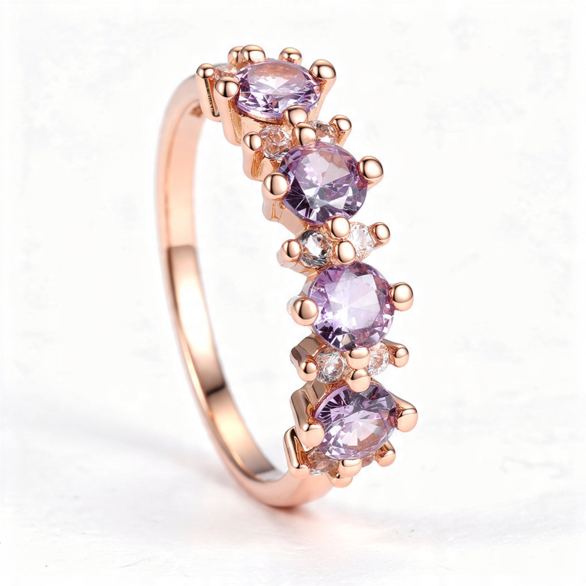 A rose gold band ring with four round lavender gemstones separated by pairs of clear round accent stones, centered on a pure white background.