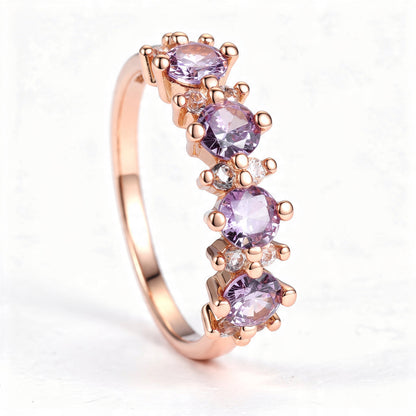 A rose gold band ring with four round lavender gemstones separated by pairs of clear round accent stones, centered on a pure white background.