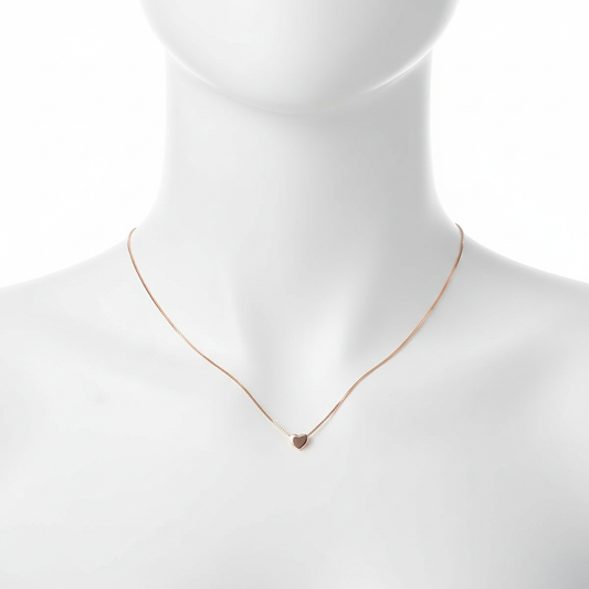 A close-up, high-resolution shot of a dainty rose gold necklace featuring a tiny, polished heart pendant on a thin box chain, displayed on a clean white jewelry mannequin against a pure white background.