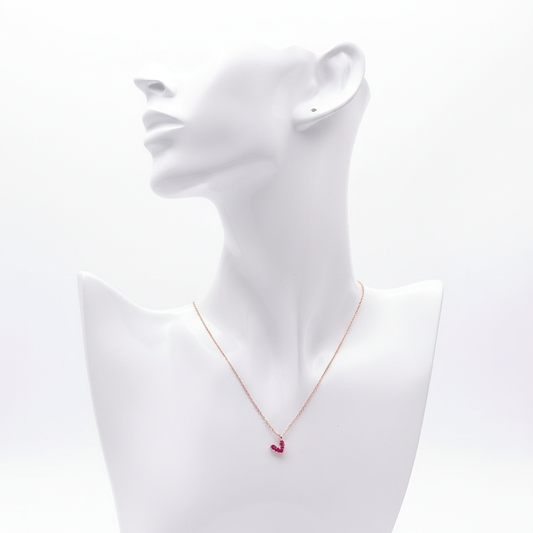 A high-resolution product shot of a dainty rose gold necklace featuring a small heart-shaped pendant pave-set with vibrant pink crystals, displayed on a sleek white bust mannequin against a pure white background.