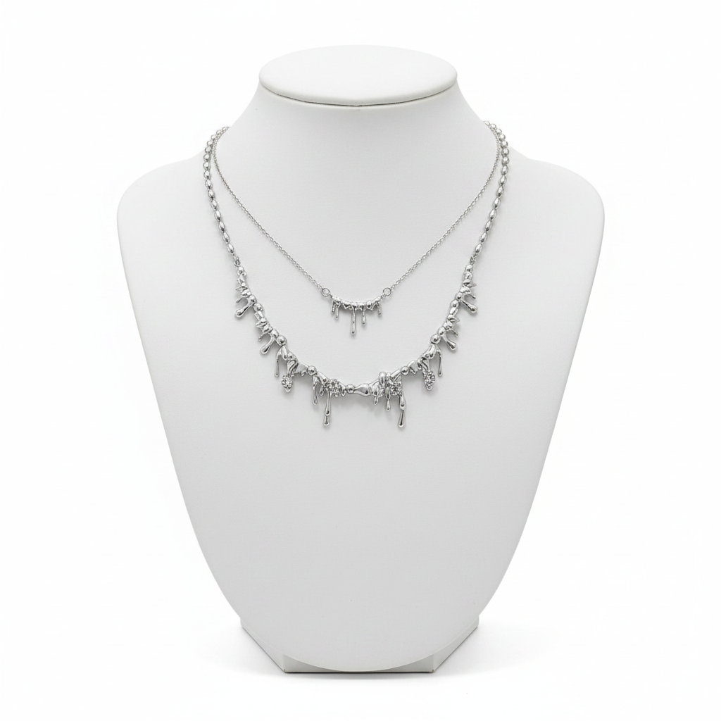 A luxury layered necklace set in silver featuring two tiers of molten dripping metal pendants on a white minimalist mannequin bust.