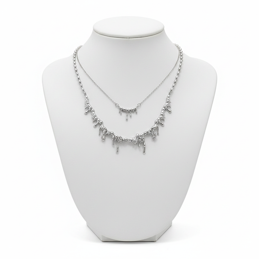 A luxury layered necklace set in silver featuring two tiers of molten dripping metal pendants on a white minimalist mannequin bust.