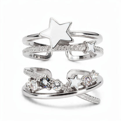 Silver celestial ring set on white background featuring white enamel stars, textured spiral bands, and clear crystal stones, stackable open adjustable rings