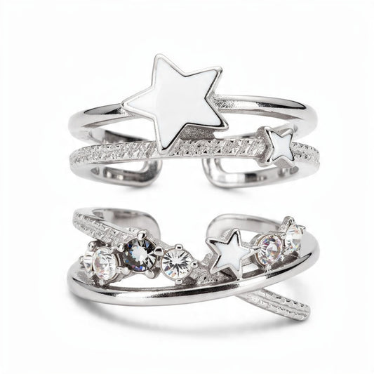 Silver celestial ring set on white background featuring white enamel stars, textured spiral bands, and clear crystal stones, stackable open adjustable rings