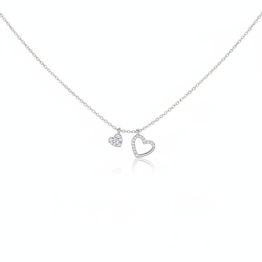 A delicate silver-toned necklace featuring two heart charms suspended from a fine cable chain. One charm is a small solid heart fully encrusted with pavé crystals, and the other is a slightly larger open-heart frame also lined with shimmering crystals. The jewelry is shown against a minimalist white background with a subtle reflection.