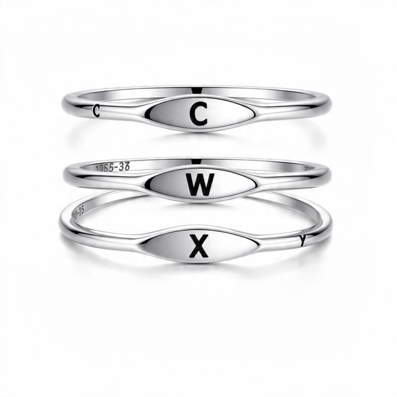 Three polished silver rings stacked vertically on a white background, each with an oval face engraved with a black capital letter: C on the top ring, W on the middle ring, and X on the bottom ring.

