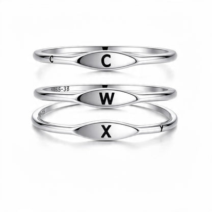 Three polished silver rings stacked vertically on a white background, each with an oval face engraved with a black capital letter: C on the top ring, W on the middle ring, and X on the bottom ring.


