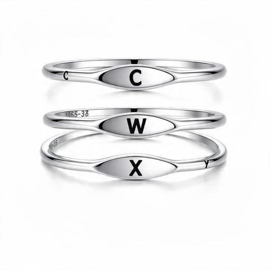 Three polished silver rings stacked vertically on a white background, each with an oval face engraved with a black capital letter: C on the top ring, W on the middle ring, and X on the bottom ring.

