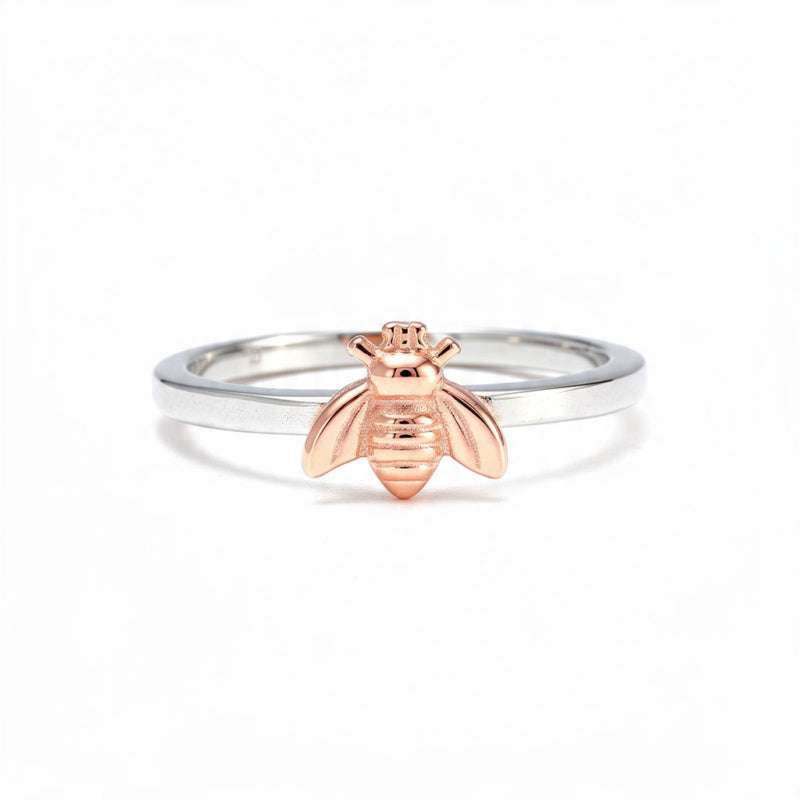 A dainty sterling silver band featuring a detailed rose gold bee charm, centered on a pure white background.