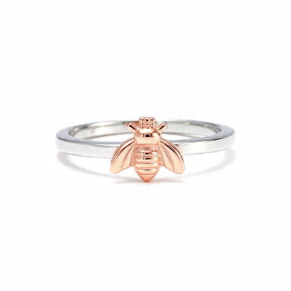 A dainty sterling silver band featuring a detailed rose gold bee charm, centered on a pure white background.
