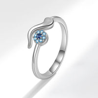 A minimalist silver-toned ring featuring a fluid, organic wave design that cradles a cluster of brilliant blue and sapphire-toned crystals, embodying a modern "Liquid Metal" and "Dopamine Stone" aesthetic.