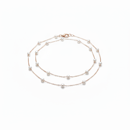 A delicate 18k gold-dipped double-layer anklet featuring evenly spaced "floating" pearls on a fine titanium steel chain, captured in a minimalist editorial style for a refined summer aesthetic.