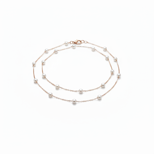 A delicate 18k gold-dipped double-layer anklet featuring evenly spaced "floating" pearls on a fine titanium steel chain, captured in a minimalist editorial style for a refined summer aesthetic.