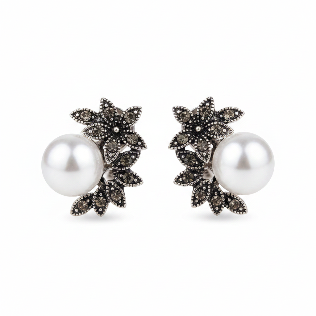 Pair of antique silver-tone stud earrings featuring an intricate floral leaf design set with dark grey marcassite stones and a large, high-luster white pearl, displayed on a clean white background.