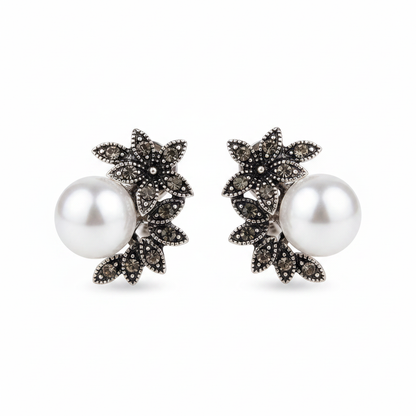 Pair of antique silver-tone stud earrings featuring an intricate floral leaf design set with dark grey marcassite stones and a large, high-luster white pearl, displayed on a clean white background.