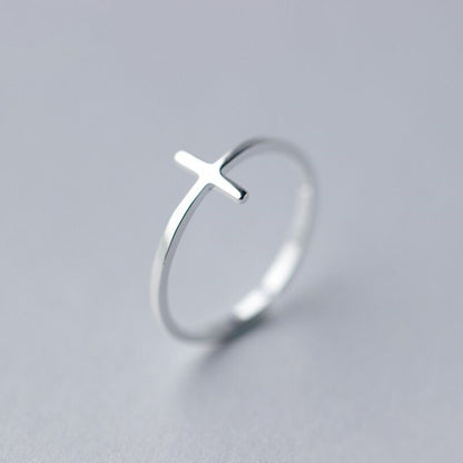 High-angle shot of a polished silver-tone sideways cross ring featuring a sleek, open-ended adjustable band design on a white background.