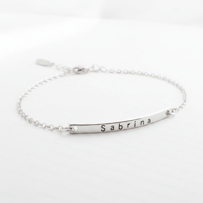 Minimalist silver chain bracelet with a curved bar engraved with the name Sabrina on a white background
