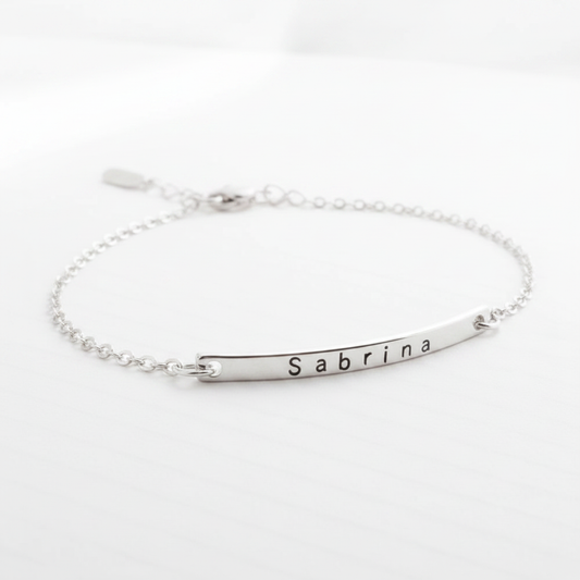 Minimalist silver chain bracelet with a curved bar engraved with the name Sabrina on a white background